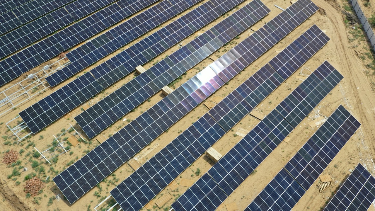 Sunlight glinting off a completed section of the array, rows running diagonally across sandy ground