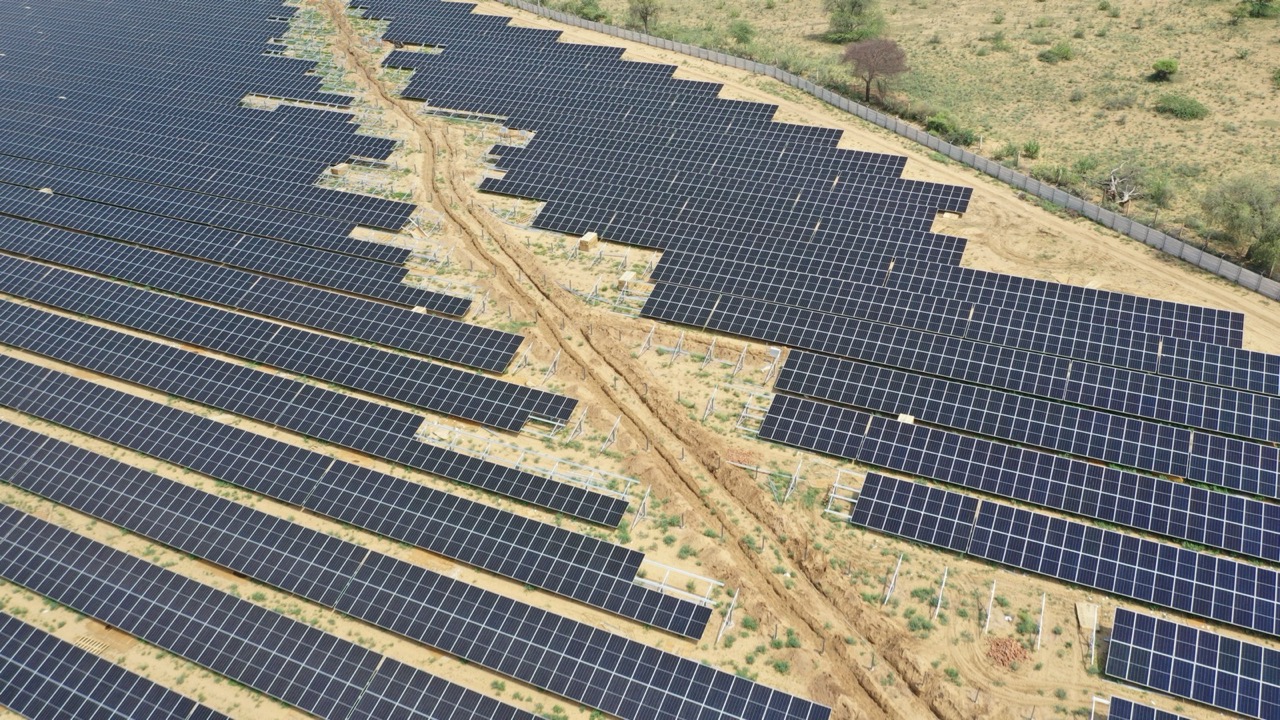Aerial view of completed module rows meeting bare mounting structures, with an access track and cable trench running between them